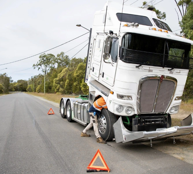 Mobile truck mechanic repairing semi truck on roadside with safety triangles deployed